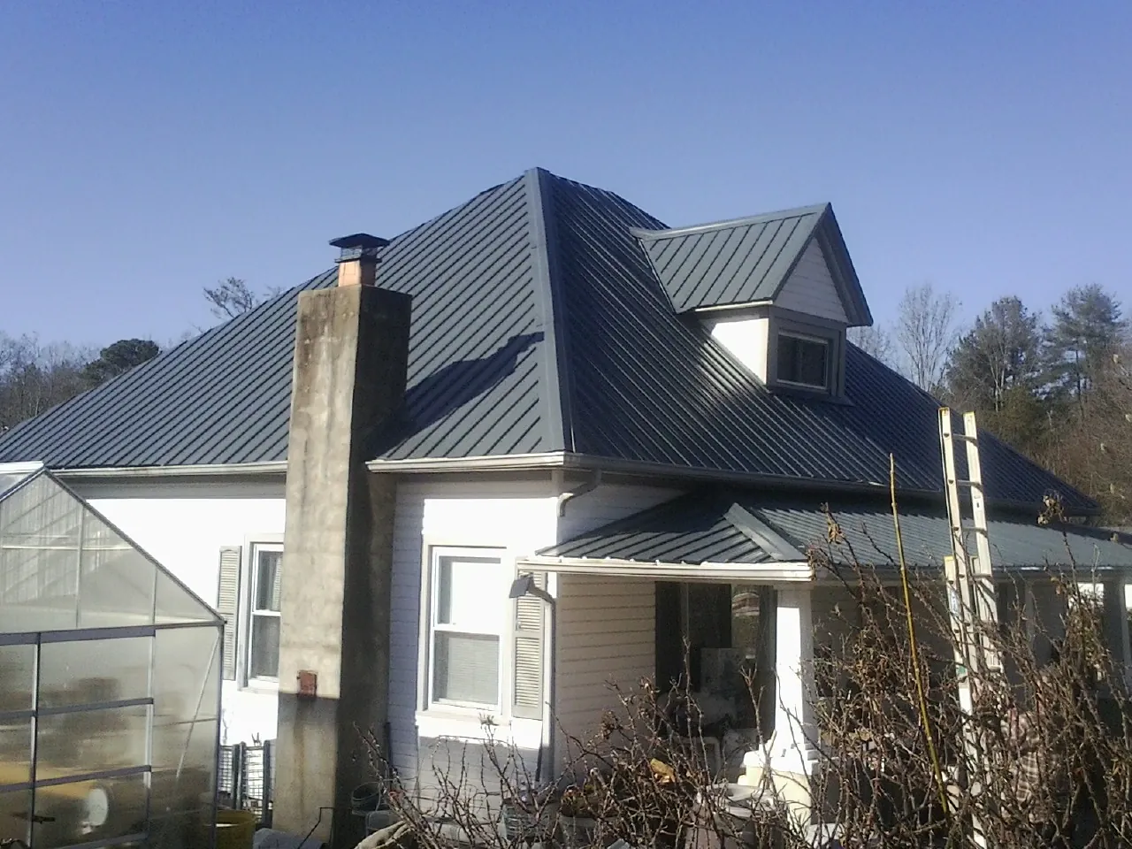 Dark blue standing seam metal roof on a white farmhouse with dormer — Slate & Tile Roof Repair by Roofing Brothers in Reform