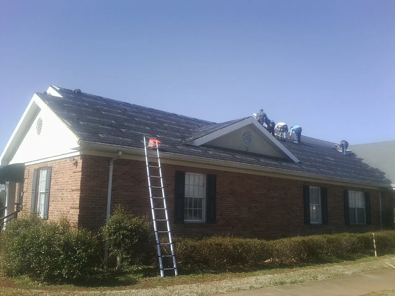 Crew tearing shingles off a brick ranch roof with a ladder set — Emergency Roof Repair work by our crew in Reform