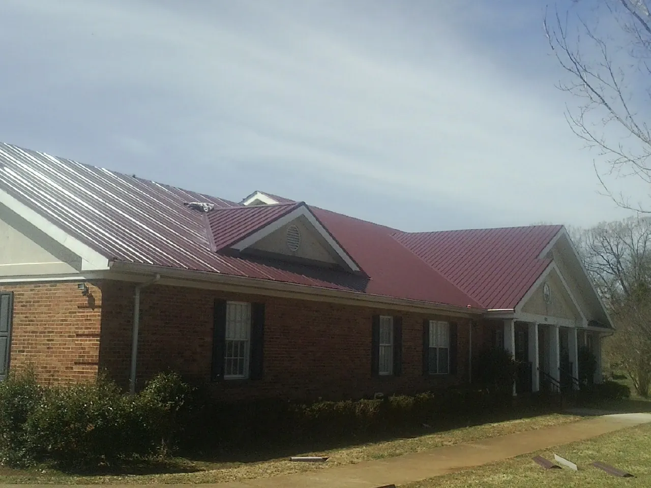 Red metal roof with gabled entries on a long brick building, from a Hail Damage Roof Repair job in Reform