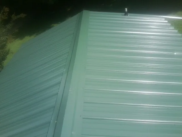New green metal panels meeting at the ridge of a roof — Flat Roof Repair work by our crew in Reform