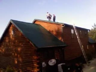 Crew on the ridge of a green metal roof on a two story log home in Reform