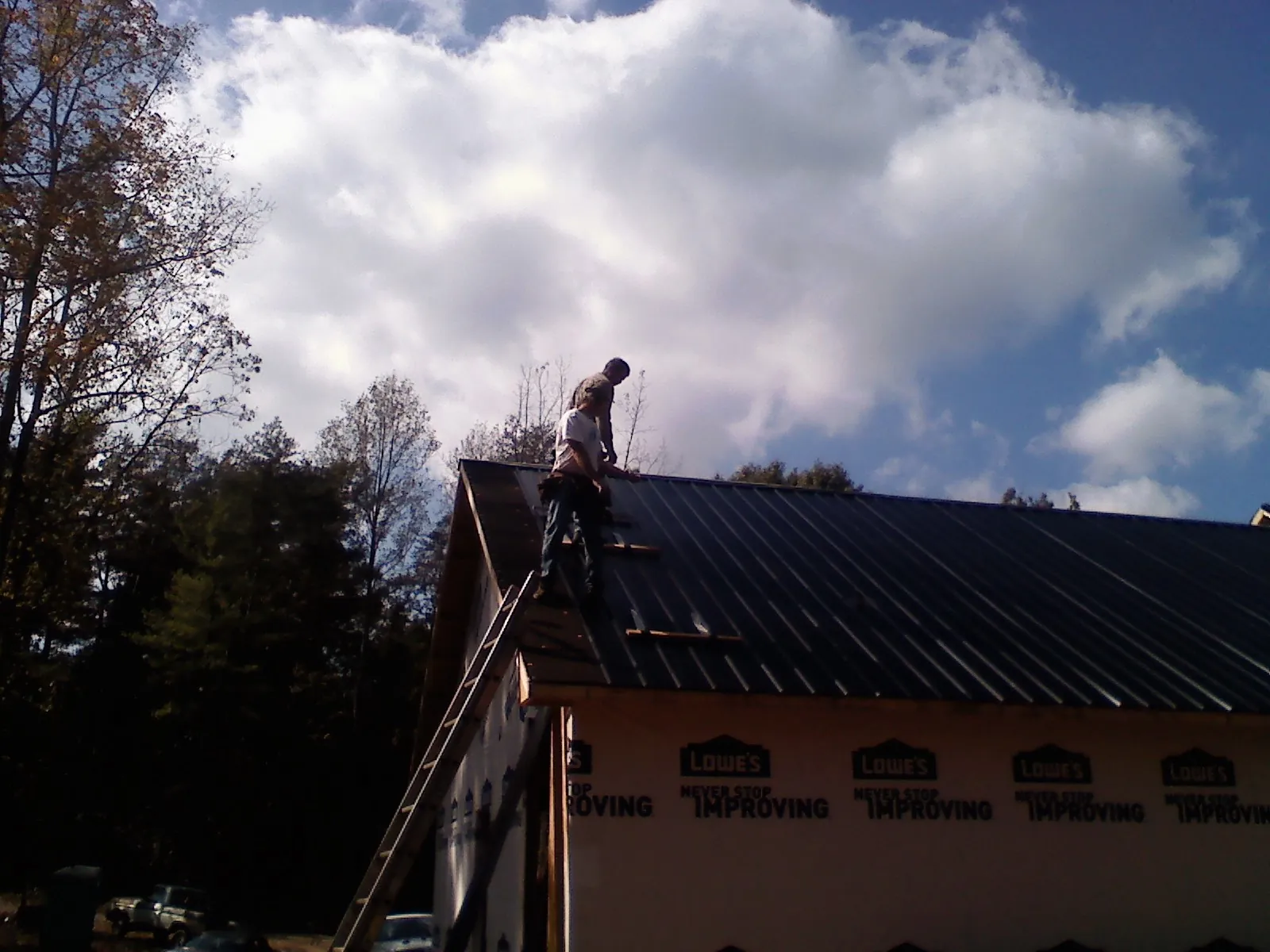 Roofer fastening dark metal panels high against a cloudy sky, from a Roof Inspection job in Reform