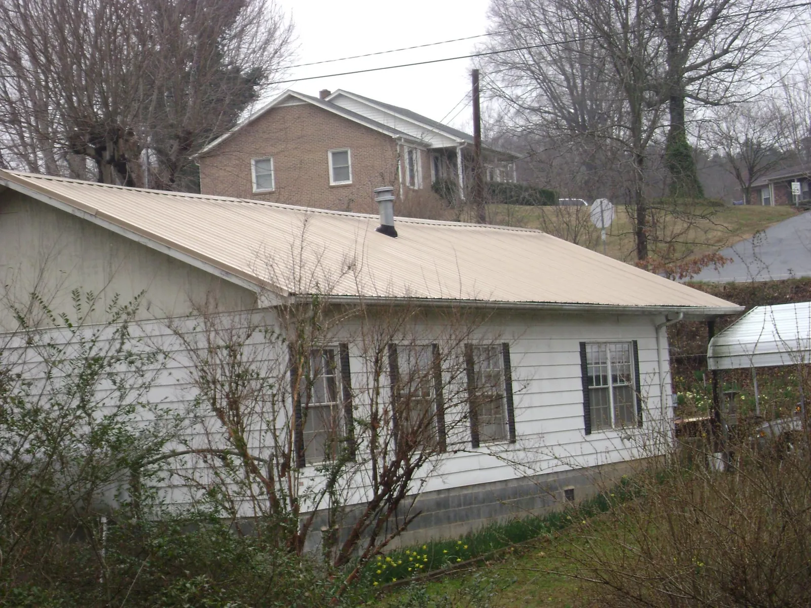 Tan metal roof on a white sided house set into a hillside — Commercial Roofing by Roofing Brothers in Reform